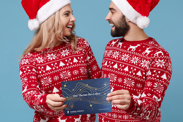 Pärchen mit Nikolausmütze im Weihnachtspullover mit Gutschein in den Händen. Pärchen mit Nikolausmütze im Weihnachtspullover mit Gutschein in den Händen.